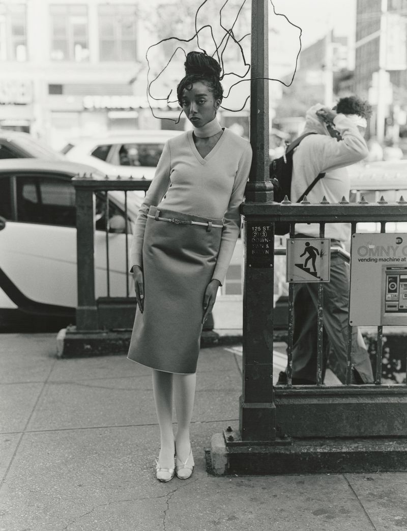 Model standing on a city sidewalk leaning against a subway entrance pole for 10 Magazine's Harlem Renaissance editorial