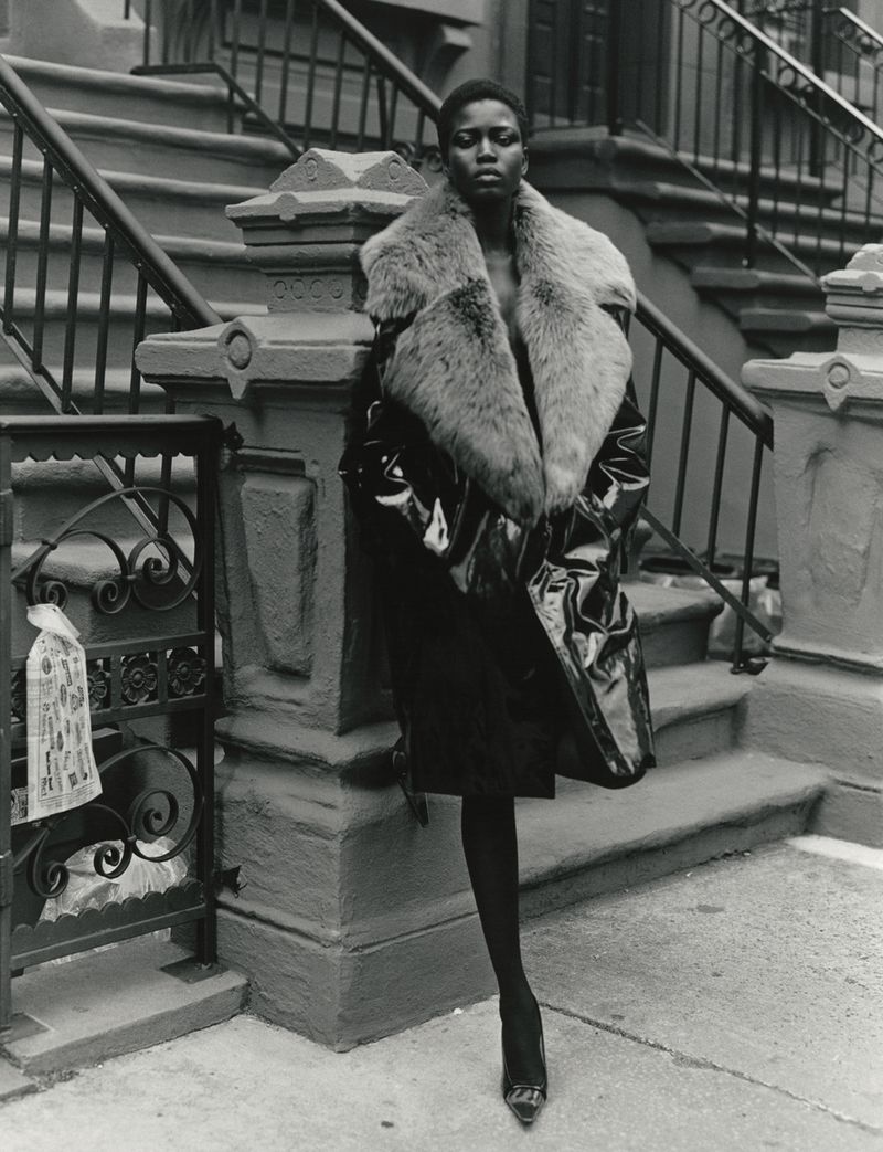 Black model wearing a glossy patent coat with a fur collar standing on brownstone steps for 10 Magazine