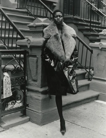 Black model wearing a glossy patent coat with a fur collar standing on brownstone steps for 10 Magazine