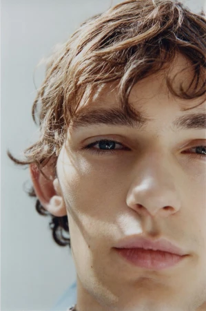 Extreme close-up portrait of a young man with wavy brown hair and natural light casting soft shadows across his face.
