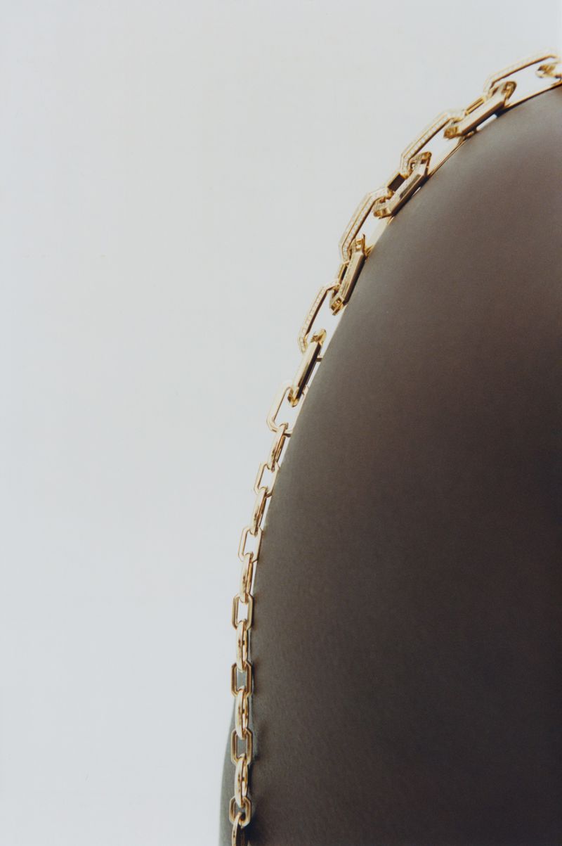Close-up shot of a delicate gold chain link necklace draped against a dark curved surface on a white background