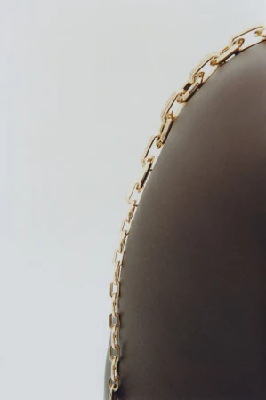 Close-up shot of a delicate gold chain link necklace draped against a dark curved surface on a white background