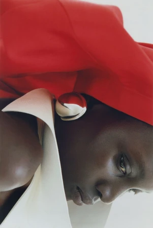 Close-up fashion portrait of a Black woman wearing a large silver earring, white collar, and vibrant red garment.