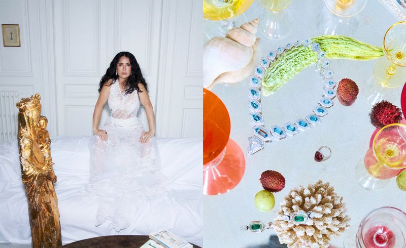 Salma Hayek in a white lace dress seated against white panels, alongside a still life of jewellery and glassware.