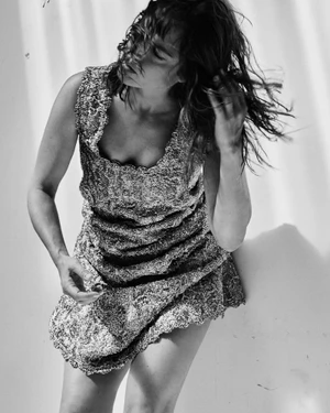Woman in patterned sleeveless dress touching her tousled hair against a bright textured background