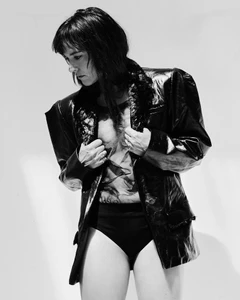 Woman wearing a shiny black blazer and high-waisted briefs against a plain white background for a Numero France project