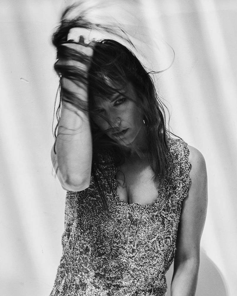 Monochrome portrait of a woman running her hand through long dark hair against a textured background for Numéro France
