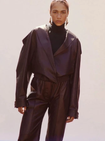 Model wearing a dark brown leather jacket and matching pants with a black turtleneck against a light neutral background.