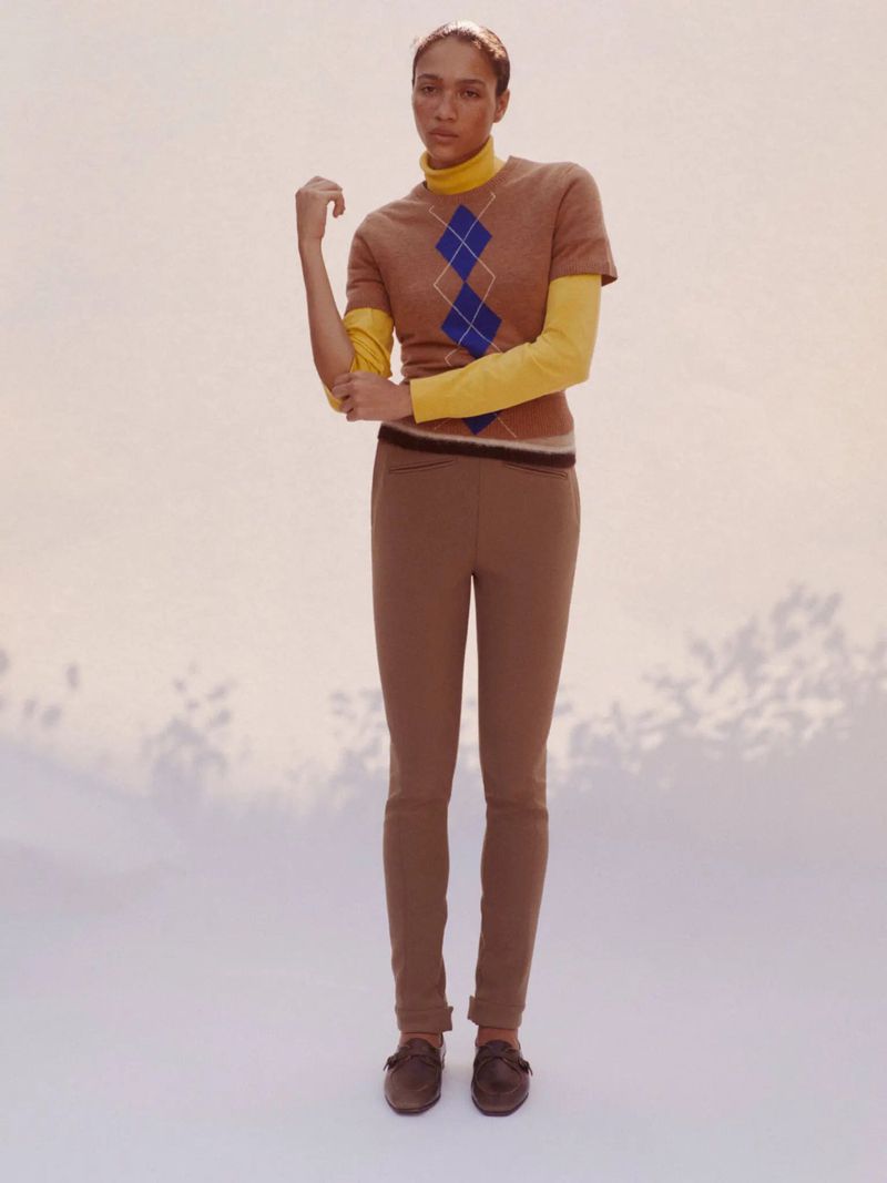 Model in brown argyle sweater and matching trousers posing against a plain backdrop with floral shadows
