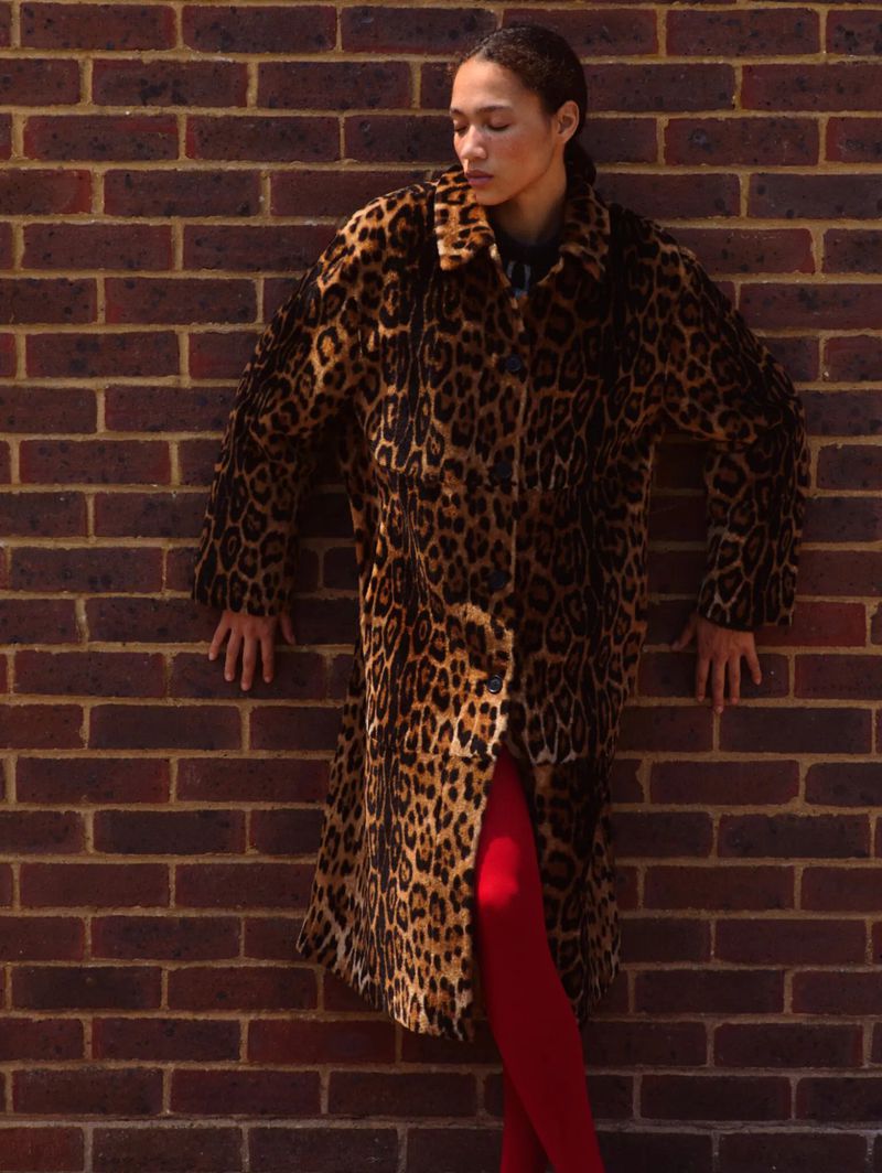 Model leaning against a red brick wall wearing a leopard print coat and red tights