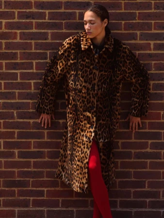 Model leaning against a red brick wall wearing a leopard print coat and red tights