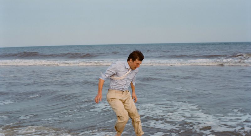Man in shirt and pants walking in ocean water at daytime. Seascape of sea with waves, horizon, and sky in the background.