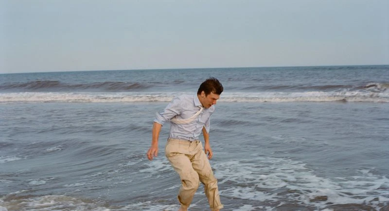 Man in shirt and pants walking in ocean water at daytime. Seascape of sea with waves, horizon, and sky in the background.
