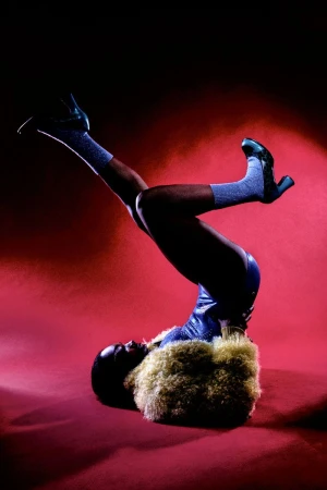 Model lying on a red background with legs raised in the air wearing shiny blue shorts, sparkly socks, and heels.