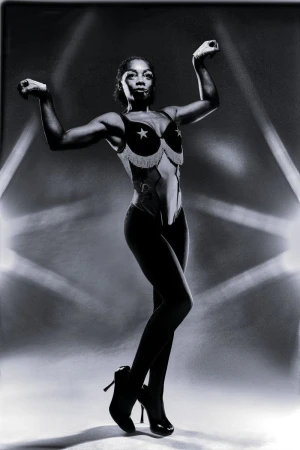 Black and white portrait of a woman posing in a star-patterned bra top and dark high heels against a dramatic lit backdrop.
