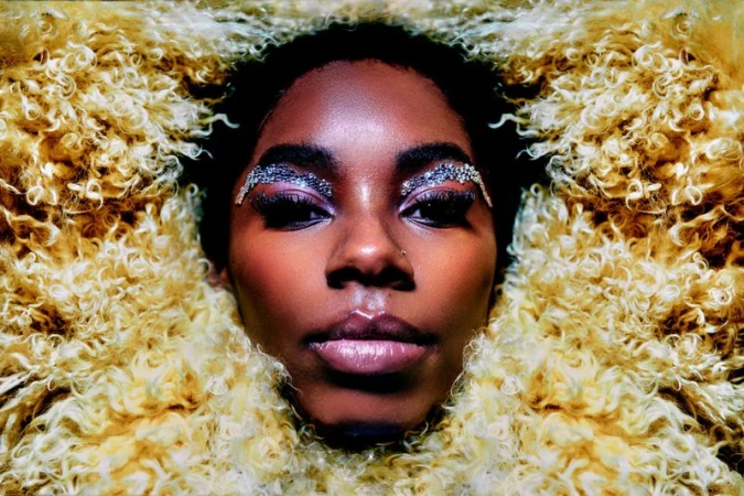 Close-up portrait of a Black woman with glittering crystal eyebrows framed by yellow textured faux fur