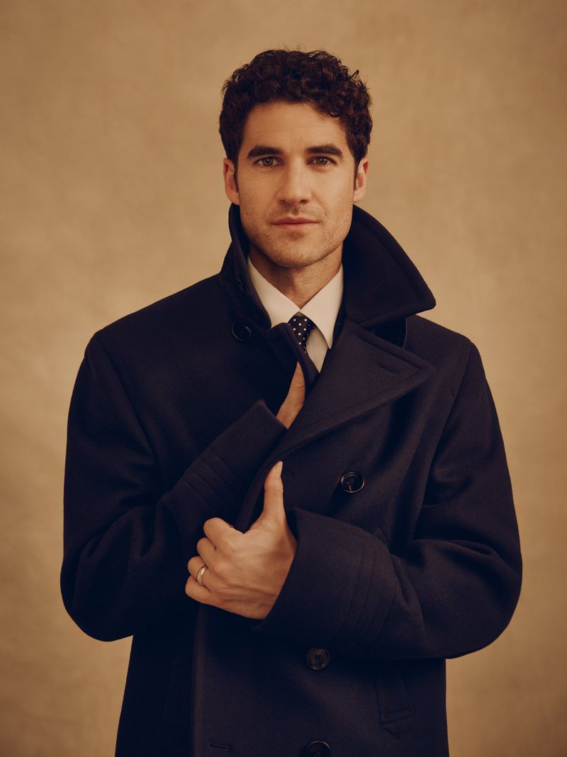Darren Criss wearing a dark blue pea coat and tie against a warm textured background for GQ Philippines editorial