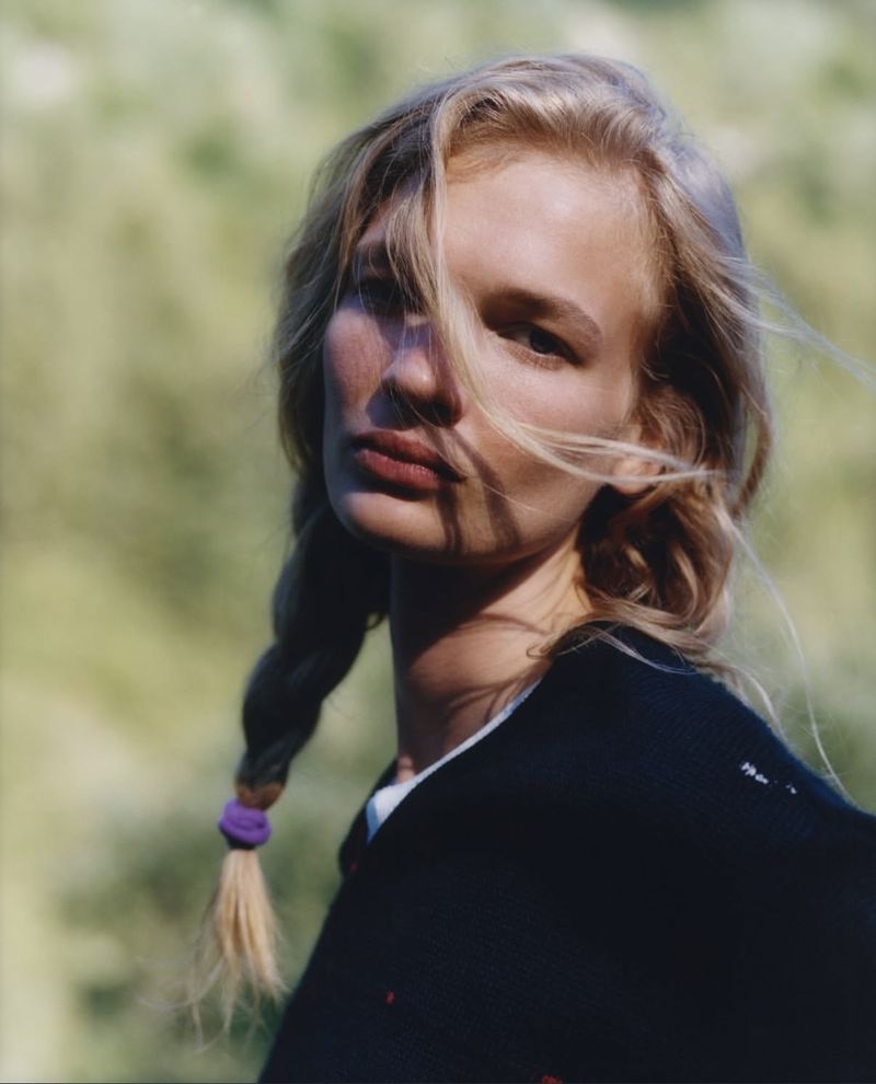 Model with blonde braided hair in a black top outdoors against a soft green background for Pop Magazine