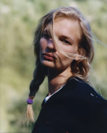 Model with blonde braided hair in a black top outdoors against a soft green background for Pop Magazine