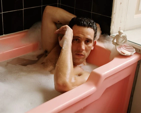 Actor Josh O Connor lying in a pink bathtub filled with soapy water for AnOther Magazine by Alasdair McLellan