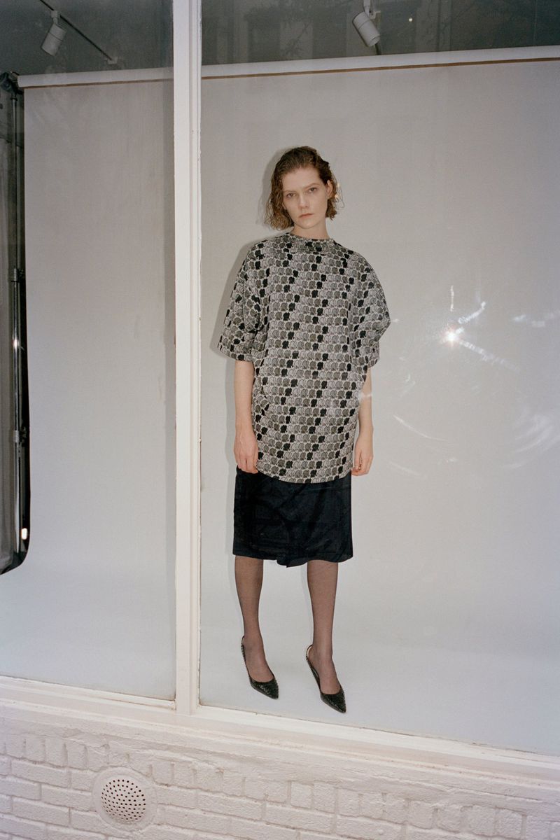 Model wearing patterned short-sleeve top and dark skirt in studio setting