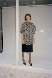 Model wearing patterned short-sleeve top and dark skirt in studio setting