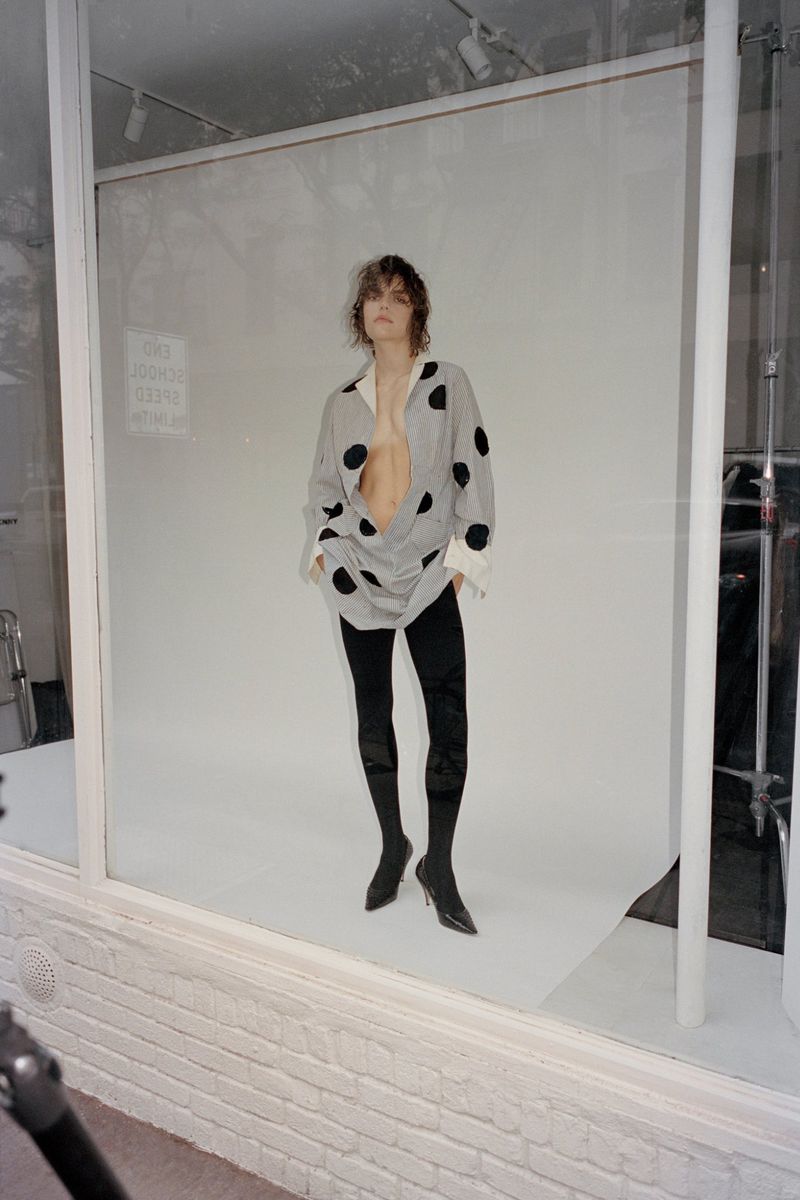 Model wearing a polka dot top and black trousers posing against a bright white seamless studio backdrop.
