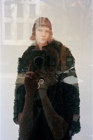 Model in a dark textured garment holding a vintage camera for a mirror reflection shot in a CDLM lookbook.