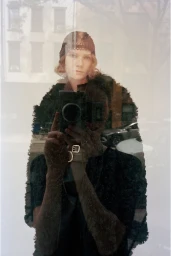 Model in a dark textured garment holding a vintage camera for a mirror reflection shot in a CDLM lookbook.