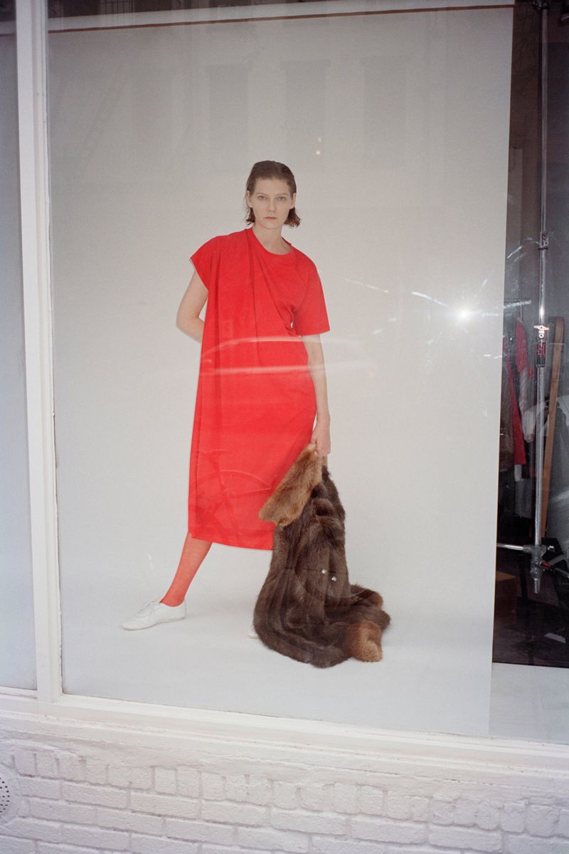 Model wearing a vibrant red dress and holding a brown fur coat against a white studio background