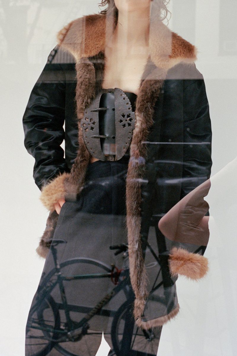Model wearing a dark jacket with brown fur trim and a decorative metal corset piece for CDLM