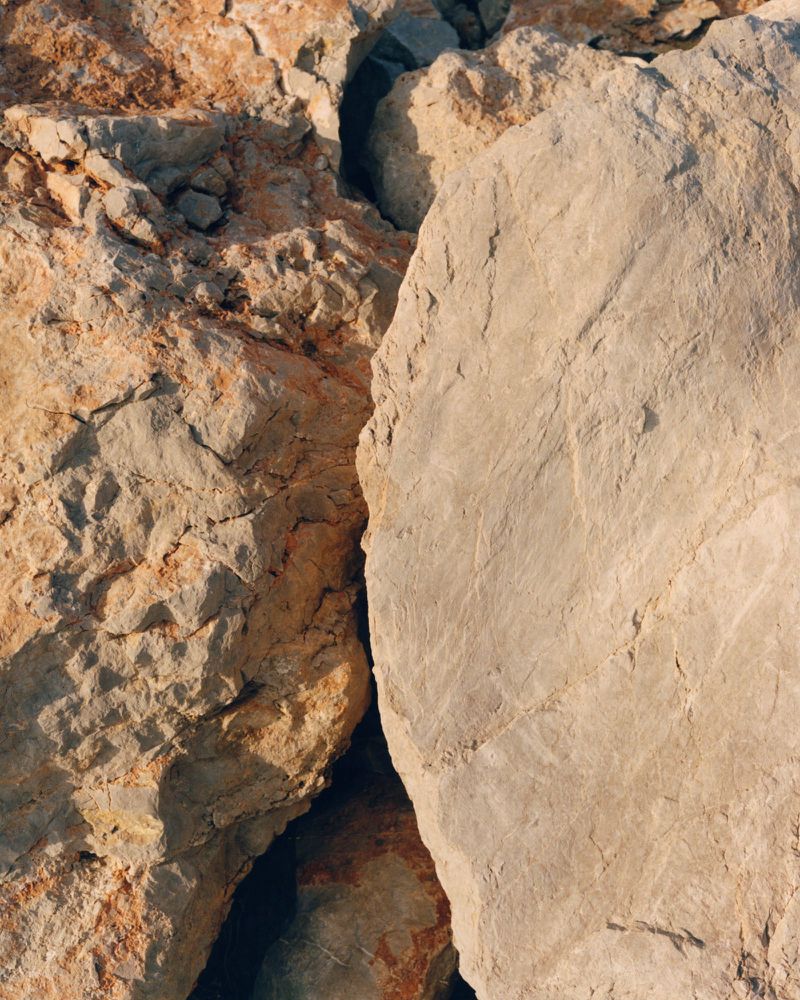 Close-up photograph of large, rough-textured rocks in shades of tan, orange, and grey. Natural rock formations, geological landscape.