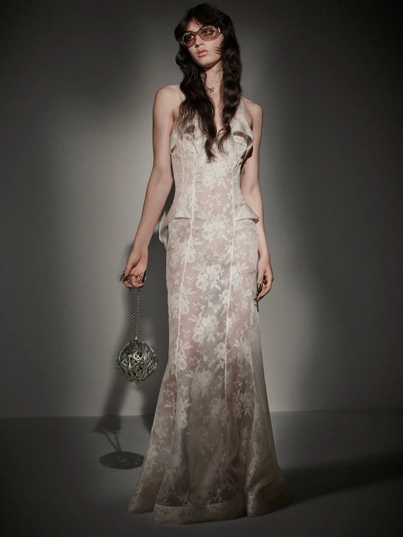 Model in lace dress wearing sunglasses holding metallic orb handbag against a grey studio backdrop