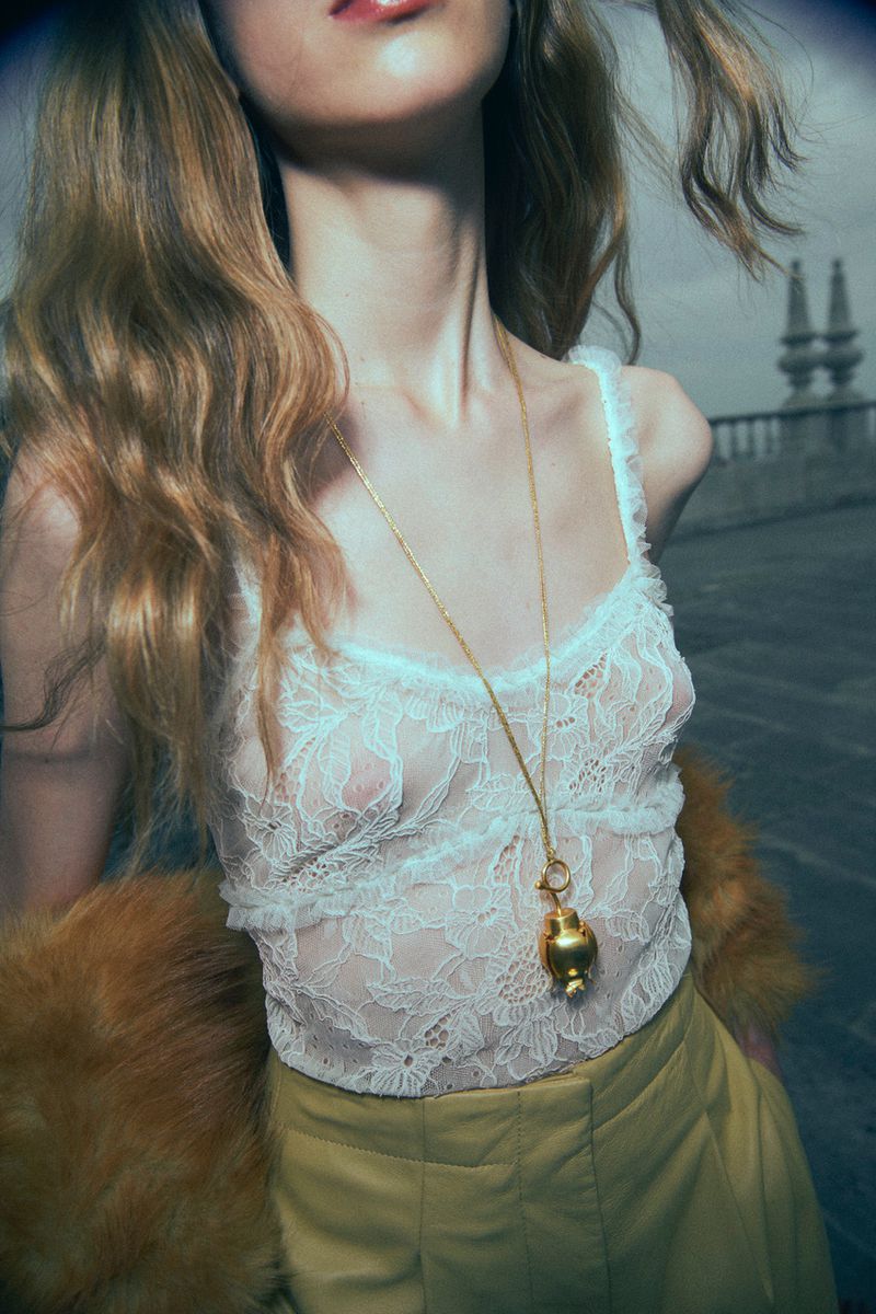 Model in white lace top and yellow trousers wearing a long gold pendant necklace outdoors