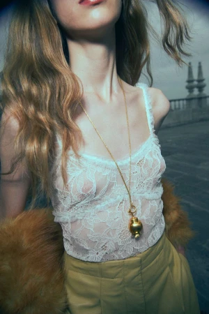 Model in white lace top and yellow trousers wearing a long gold pendant necklace outdoors
