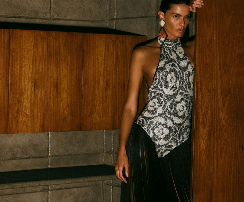 Model Isabeli Fontana wearing a halter top and black skirt leaning against wood paneling in a fashion editorial by Lufre.