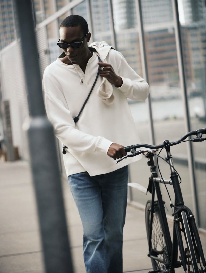 Man wearing sunglasses and white long-sleeve shirt walking with a bicycle outdoors