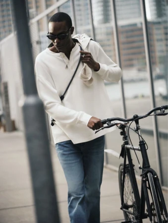Man wearing sunglasses and white long-sleeve shirt walking with a bicycle outdoors