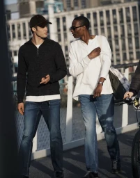 Two men walking and talking outdoors in a city setting wearing denim jeans and casual shirts