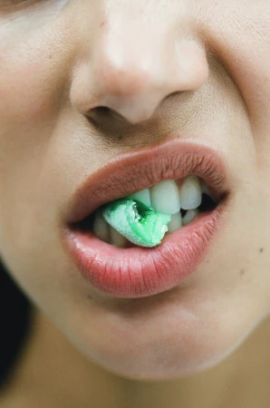 Close-up of a person's lower face biting a piece of green marshmallow candy between teeth
