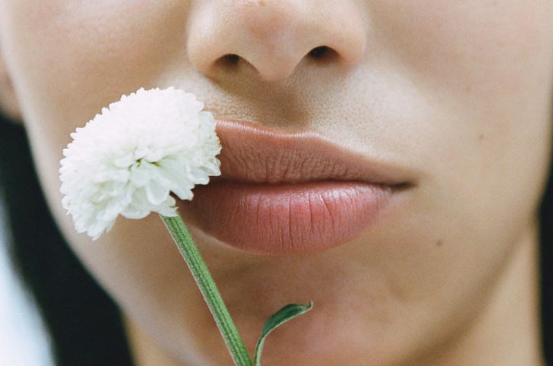 Close-up portrait of a person holding a white flower stem near their lips, photographed by Estévez and Belloso.