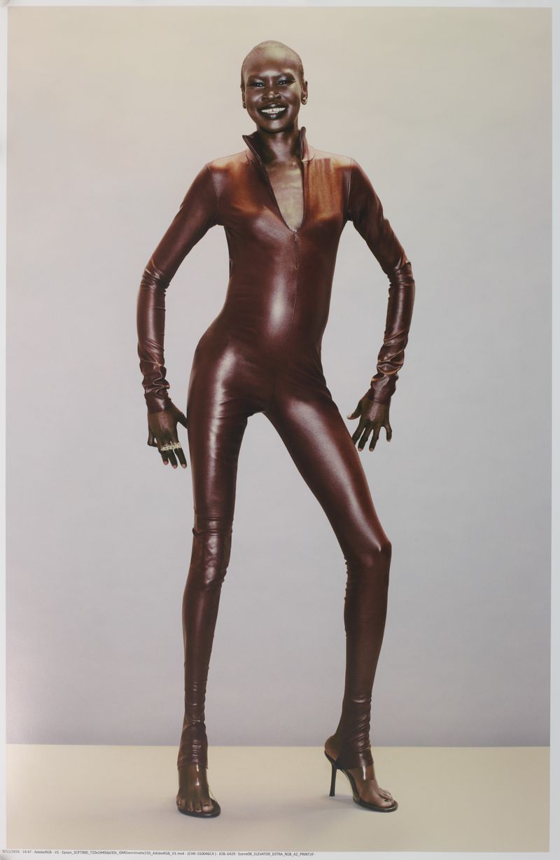Model wearing a glossy dark brown leather catsuit against a seamless grey backdrop for Mowalola
