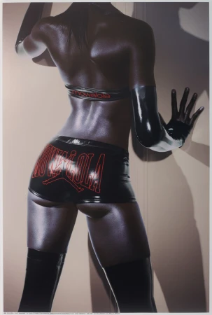 Rear view of a model in black latex shorts and top with red branding leaning against a neutral wall