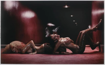Two models posing together on a dark red carpeted hallway floor in a low light campaign shoot for Mowalola