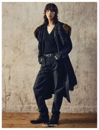 Model Song Ah Woo wearing a black coat and trousers standing against a textured concrete wall.