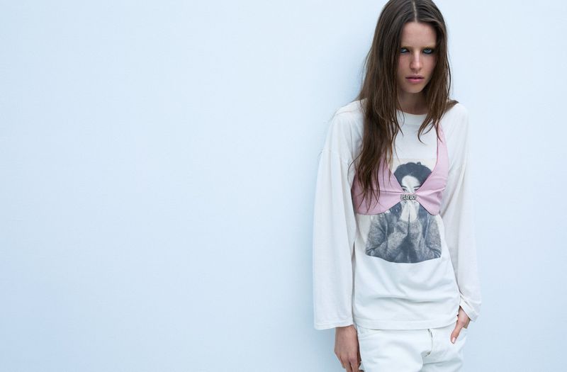 Model Libby Taverner wearing a white t-shirt and pink crop top against a light grey seamless studio backdrop.