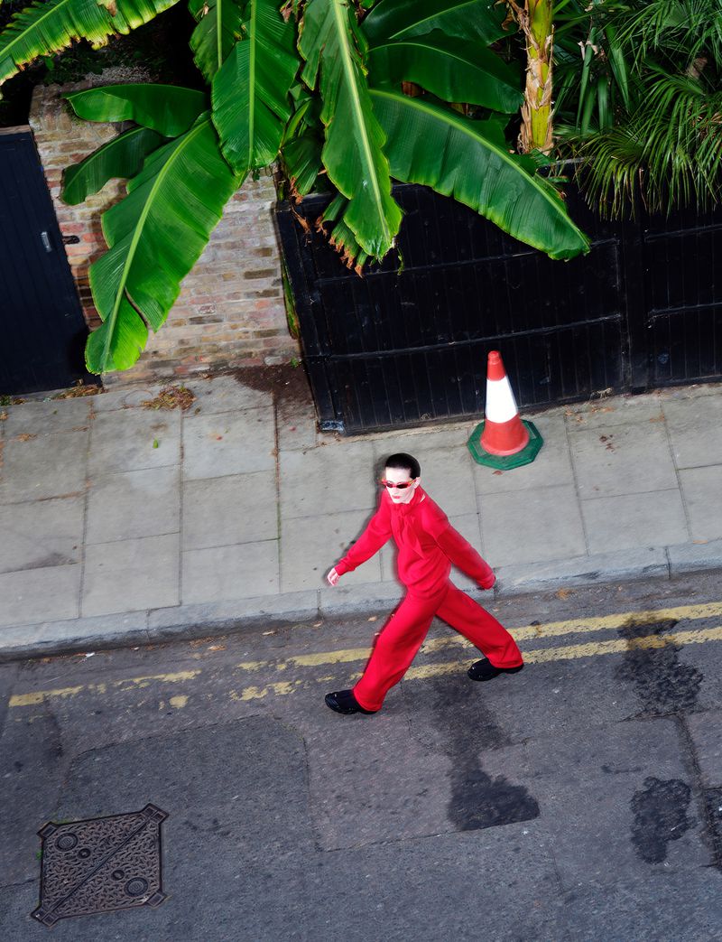 Model walking on street in red tracksuit with traffic cone and banana tree overhead