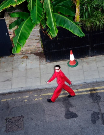 Model walking on street in red tracksuit with traffic cone and banana tree overhead