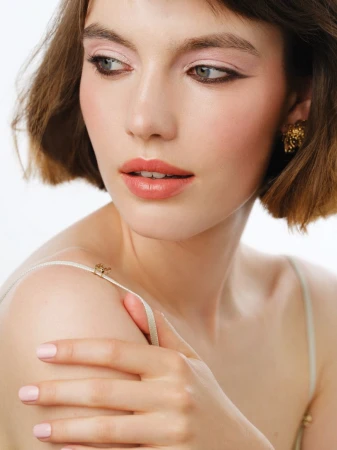 Close-up portrait of a woman with short brown hair, pink eyeshadow, and natural coral lipstick against a plain white background