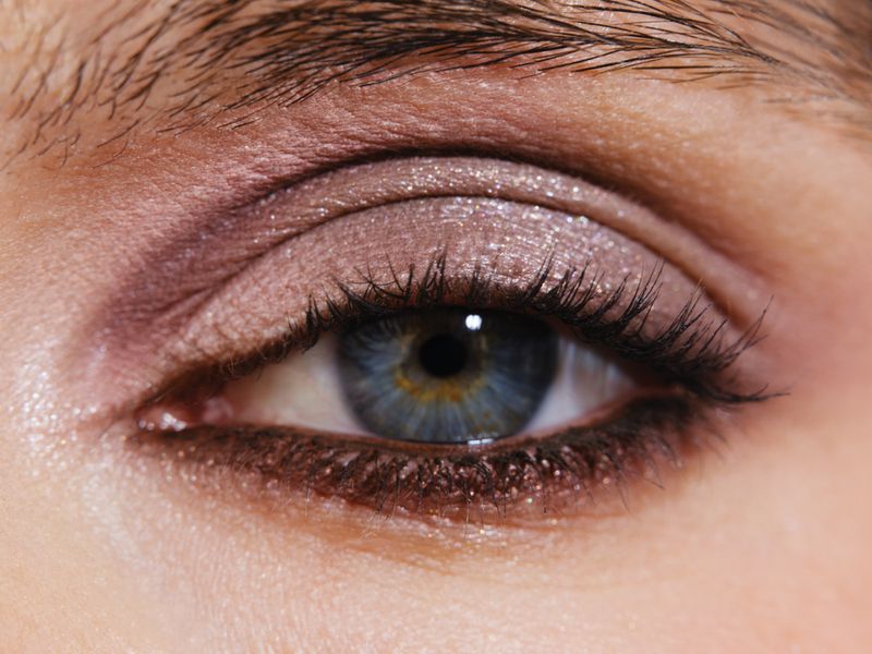 Close-up macro shot of a blue human eye with shimmer eyeshadow and defined eyelashes for Mojeh Magazine.